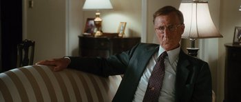 Movie still from “W.” (2008), directed by Oliver Stone – An older man sitting on a couch in a room; Close Up shot, Over the shoulder angle