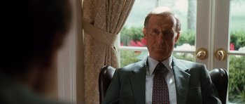Movie still from “W.” (2008), directed by Oliver Stone – An older man wearing a suit and tie sitting in a chair in front of a window; Close Up shot, Low angle