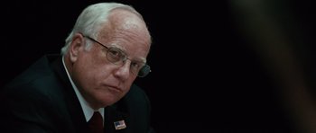Movie still from “W.” (2008), directed by Oliver Stone – An older man wearing glasses and a suit; Close Up shot, Over the shoulder angle