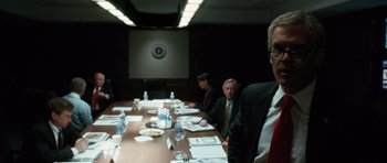 Movie still from “W.” (2008), directed by Oliver Stone – A group of people sitting at a table in front of a projector screen; Medium shot, Over the shoulder angle