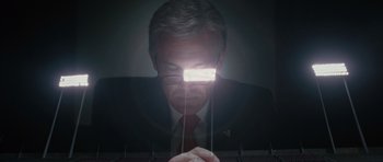 Movie still from “W.” (2008), directed by Oliver Stone – A man in a suit and glasses is looking down at a light; Close Up shot, Low angle