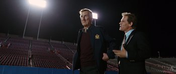 Movie still from “W.” (2008), directed by Oliver Stone – Two men standing next to each other on a field; Medium shot, Low angle