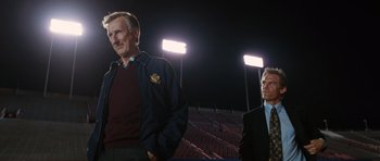 Movie still from “W.” (2008), directed by Oliver Stone – Two men standing next to each other on a field; Medium shot, Low angle