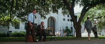 Movie still from “W.” (2008), directed by Oliver Stone – A man sitting on a park bench next to a tree; Wide shot, Low angle
