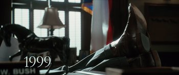 Movie still from “W.” (2008), directed by Oliver Stone – A person's foot on top of a table in front of a window; Medium shot, Low angle