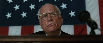 Movie still from “W.” (2008), directed by Oliver Stone – An older man wearing glasses in front of an american flag; Close Up shot, Low angle