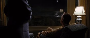 Movie still from “W.” (2008), directed by Oliver Stone – An older man sitting in a chair looking out a window at the moon; Wide shot, High angle