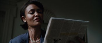 Movie still from “W.” (2008), directed by Oliver Stone – A woman reading a newspaper while sitting in a chair; Close Up shot, Low angle