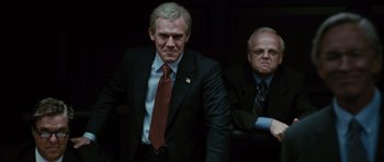 Movie still from “W.” (2008), directed by Oliver Stone – A man in a suit standing next to another man in a suit; Medium shot, Low angle