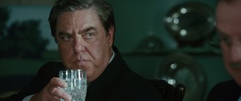 Movie still from “W.” (2008), directed by Oliver Stone – An older man holding a wine glass in his hand; Close Up shot, Over the shoulder angle