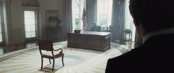 Movie still from “W.” (2008), directed by Oliver Stone – A man sitting at a desk in the oval office of the white house; Wide shot, High angle