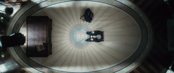 Movie still from “W.” (2008), directed by Oliver Stone – Two people are standing in a rotunda looking up at the ceiling; Wide shot, Overhead angle