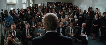 Movie still from “W.” (2008), directed by Oliver Stone – A crowd of people sitting and standing in a room; Medium shot, Over the shoulder angle