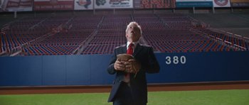 Movie still from “W.” (2008), directed by Oliver Stone – A man in a suit and tie holding a baseball glove; Medium shot, Low angle