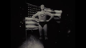 Movie still from “Waiting for Superman” (2010), directed by Davis Guggenheim – A man dressed as superman standing in front of an american flag; Wide shot, Low angle