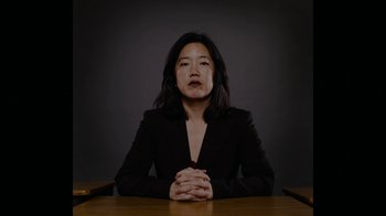 Movie still from “Waiting for Superman” (2010), directed by Davis Guggenheim – A woman sitting at a table with her hands crossed; Medium shot, Low angle