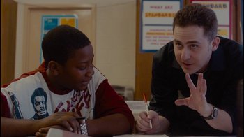 Movie still from “Waiting for Superman” (2010), directed by Davis Guggenheim – Two people sitting at a table and one is writing on a piece of paper; Medium shot, Over the shoulder angle