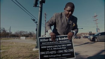 Movie still from “Waiting for Superman” (2010), directed by Davis Guggenheim – A man holding a sign that reads " miller - murray academy mathematics & business; Medium shot, Low angle