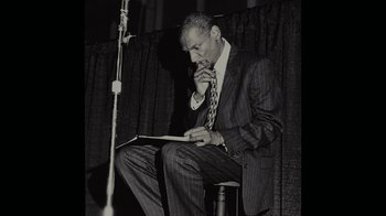 Movie still from “Waiting for Superman” (2010), directed by Davis Guggenheim – A man sitting on a chair looking at a book; Medium shot, Low angle