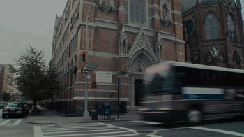 Movie still from “Waiting for Superman” (2010), directed by Davis Guggenheim – A bus driving down a street next to a building; Extreme Wide shot, Low angle