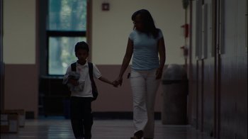 Movie still from “Waiting for Superman” (2010), directed by Davis Guggenheim – A woman and a boy holding hands while walking down a hallway; Wide shot, Low angle
