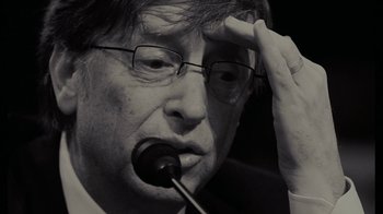 Movie still from “Waiting for Superman” (2010), directed by Davis Guggenheim – An older man wearing glasses and holding a pipe in his mouth; Close Up shot, Over the shoulder angle