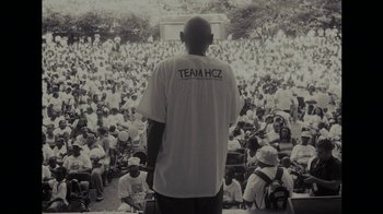 Movie still from “Waiting for Superman” (2010), directed by Davis Guggenheim – A black and white photo of a man standing in front of a crowd; Extreme Wide shot, Over the shoulder angle