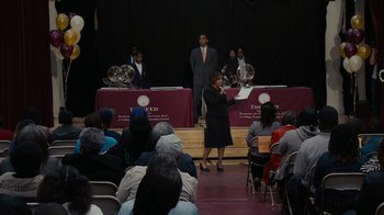 Movie still from “Waiting for Superman” (2010), directed by Davis Guggenheim – A group of people sitting in front of a microphone; Extreme Wide shot, High angle
