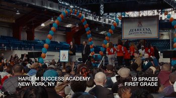Movie still from “Waiting for Superman” (2010), directed by Davis Guggenheim – A group of people sitting in front of a crowd; Extreme Wide shot, High angle