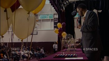 Movie still from “Waiting for Superman” (2010), directed by Davis Guggenheim – A man standing in front of a table with balloons and a menorah on top of it; Wide shot, High angle