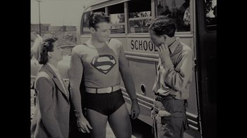 Movie still from “Waiting for Superman” (2010), directed by Davis Guggenheim – A man wearing a superman shirt talking to another man in front of a school bus; Medium shot, Over the shoulder angle