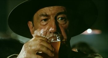 Movie still from “Wake in Fright” (1971), directed by Ted Kotcheff – A person holding a glass of beer; Close Up shot, Over the shoulder angle