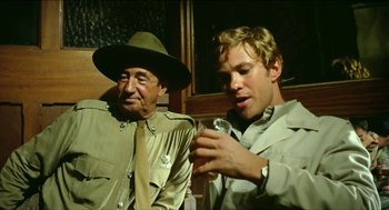 Movie still from “Wake in Fright” (1971), directed by Ted Kotcheff – A man and an old man sitting next to each other; Medium shot, Over the shoulder angle