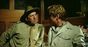 Movie still from “Wake in Fright” (1971), directed by Ted Kotcheff – A man in a hat talking to another man in a hat; Medium shot, Over the shoulder angle