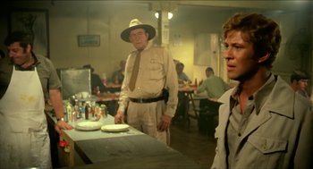 Movie still from “Wake in Fright” (1971), directed by Ted Kotcheff – A man in a hat and a man in a uniform; Medium shot, Over the shoulder angle