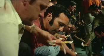Movie still from “Wake in Fright” (1971), directed by Ted Kotcheff – A group of men sitting in a row looking at their cell phones; Medium shot, High angle