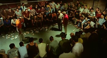 Movie still from “Wake in Fright” (1971), directed by Ted Kotcheff – A group of people sitting in front of a crowd; Wide shot, High angle