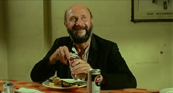 Movie still from “Wake in Fright” (1971), directed by Ted Kotcheff – A man sitting at a table with a plate of food and a drink; Medium shot, Low angle