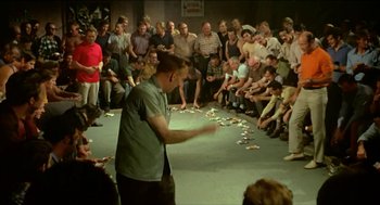 Movie still from “Wake in Fright” (1971), directed by Ted Kotcheff – A man standing in front of a crowd of onlookers; Wide shot, High angle