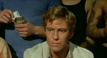 Movie still from “Wake in Fright” (1971), directed by Ted Kotcheff – A man with blonde hair and a white shirt is looking at the camera; Close Up shot, High angle