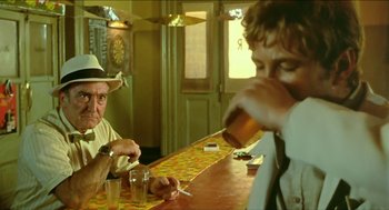 Movie still from “Wake in Fright” (1971), directed by Ted Kotcheff – Two men sitting at a bar drinking and smoking cigarettes; Medium shot, Over the shoulder angle