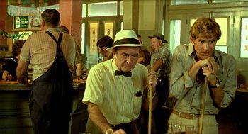 Movie still from “Wake in Fright” (1971), directed by Ted Kotcheff – An older man in a hat and a bow tie holding a pool cue; Medium shot, Over the shoulder angle