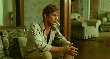 Movie still from “Wake in Fright” (1971), directed by Ted Kotcheff – A man sitting on the ground with a cigarette in his mouth; Medium shot, Over the shoulder angle