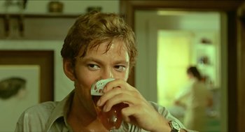 Movie still from “Wake in Fright” (1971), directed by Ted Kotcheff – A young man drinking a beer from a glass; Close Up shot, Over the shoulder angle