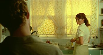 Movie still from “Wake in Fright” (1971), directed by Ted Kotcheff – A man and a woman in a kitchen with yellow curtains; Medium shot, Over the shoulder angle
