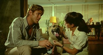 Movie still from “Wake in Fright” (1971), directed by Ted Kotcheff – A man and a woman sitting on a couch with a dog; Medium shot, Over the shoulder angle