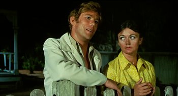 Movie still from “Wake in Fright” (1971), directed by Ted Kotcheff – A man and a woman standing next to each other in front of a wooden fence; Medium shot, Low angle
