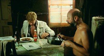 Movie still from “Wake in Fright” (1971), directed by Ted Kotcheff – Two men sitting at a table with a bowl of food; Medium shot, Low angle
