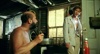Movie still from “Wake in Fright” (1971), directed by Ted Kotcheff – A man with a beard is holding a pan and looking at another man; Medium shot, Over the shoulder angle