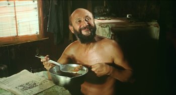 Movie still from “Wake in Fright” (1971), directed by Ted Kotcheff – A man with a beard is holding a bowl of food; Medium shot, Low angle